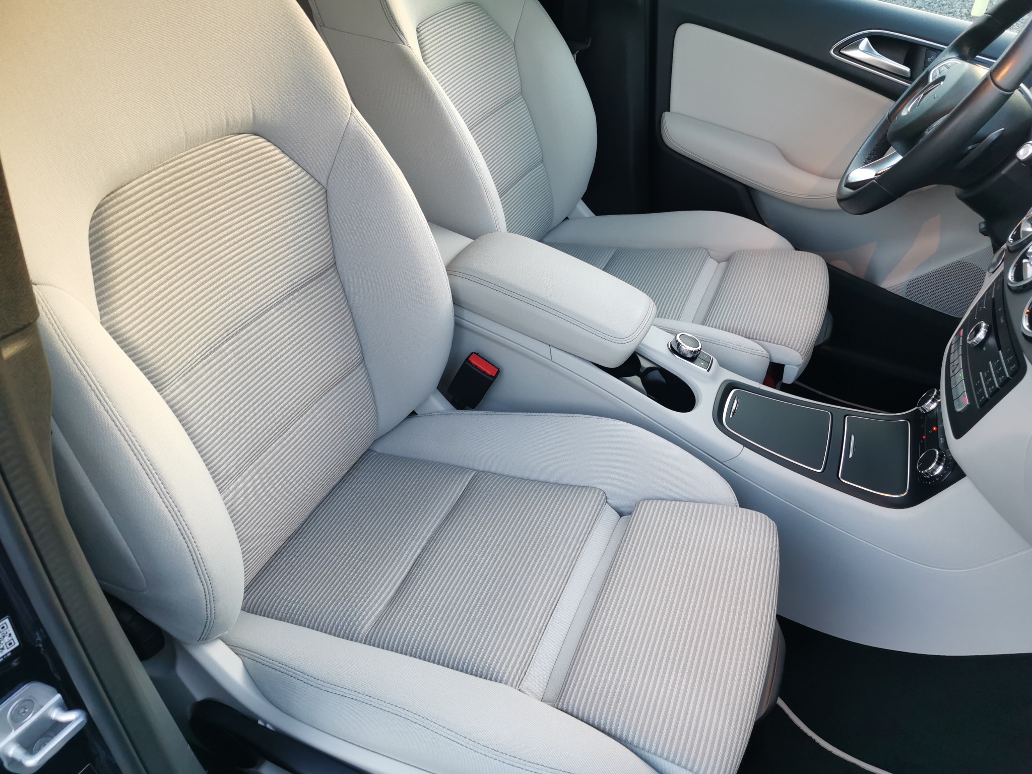 Jasne, materiałowe fotele w samochodzie osobowym, widoczne z perspektywy pasażera, z elementami deski rozdzielczej i kierownicy. Czyste wnętrze z detalami wykończenia w jasnej skórze.