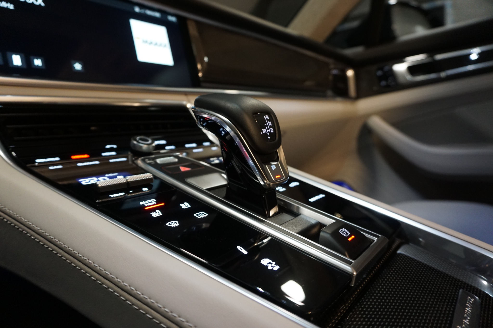 Wnętrze luksusowego samochodu z widocznym panelem sterowania i dźwignią zmiany biegów w pozycji P, podświetlone przyciski funkcyjne.