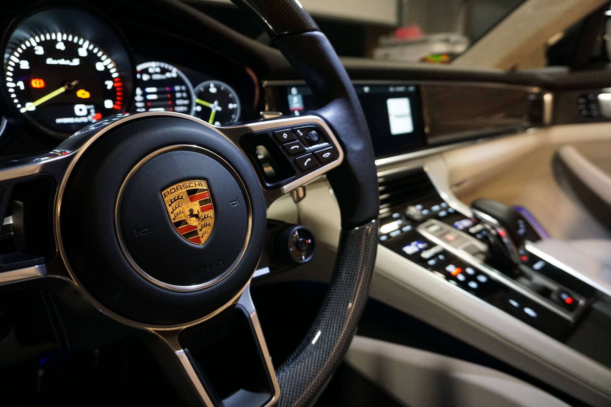 Wnętrze samochodu Porsche Panamera: kierownica z logo, deska rozdzielcza z wyświetlaczami i panelem sterowania, widoczne detale wykończenia z włókna węglowego.