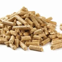 Stos brązowych, cylindrycznych granulek biopaliwa na białym tle, o nieregularnej fakturze i widocznych włóknach drzewnych.