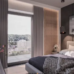 Nowoczesna sypialnia z łóżkiem w odcieniach szarości, widokiem na miasto z balkonu i dekoracjami w postaci grafik drzew oraz wazonu z kwiatami.