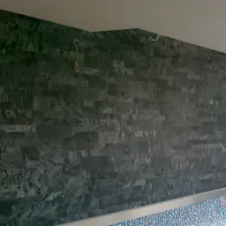 Ściana wykończona ciemnym, nieregularnym kamieniem w basenie wewnętrznym, z widocznym fragmentem instalacji elektrycznej na suficie.