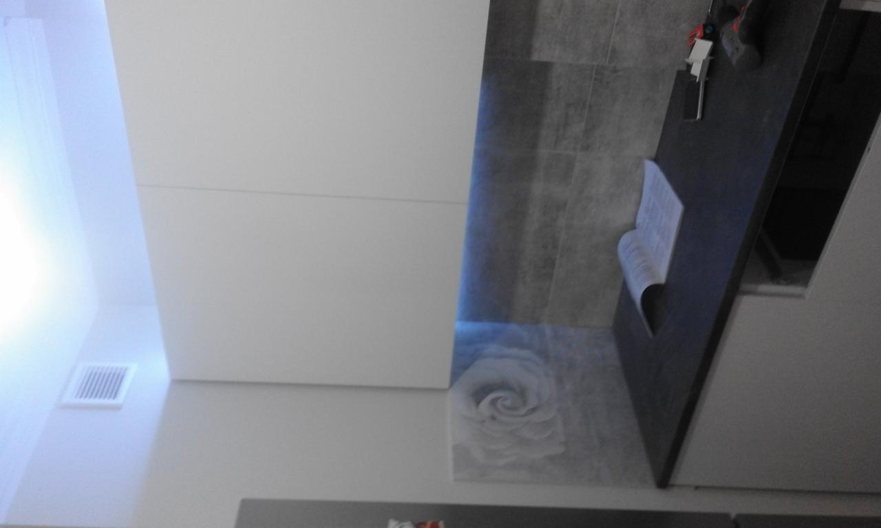 Fragment łazienki z białą szafką, szarą płytką z motywem róży i elementami montażowymi na blacie.