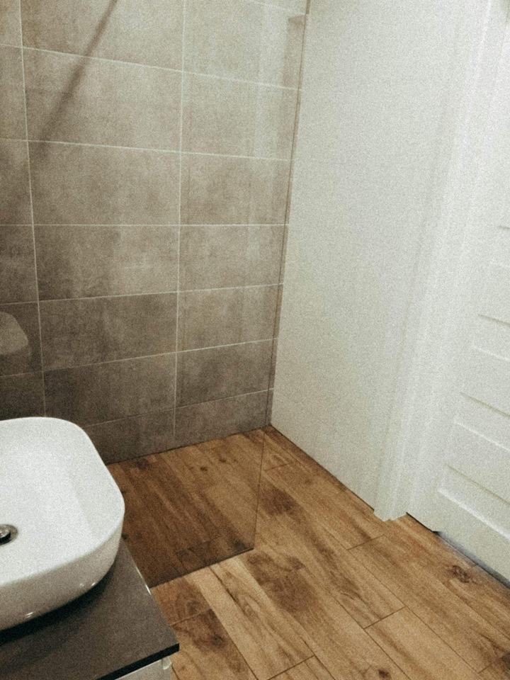 Umywalka nablatowa na szarej szafce w łazience z drewnopodobną podłogą i szarymi płytkami na ścianie, widok z góry.