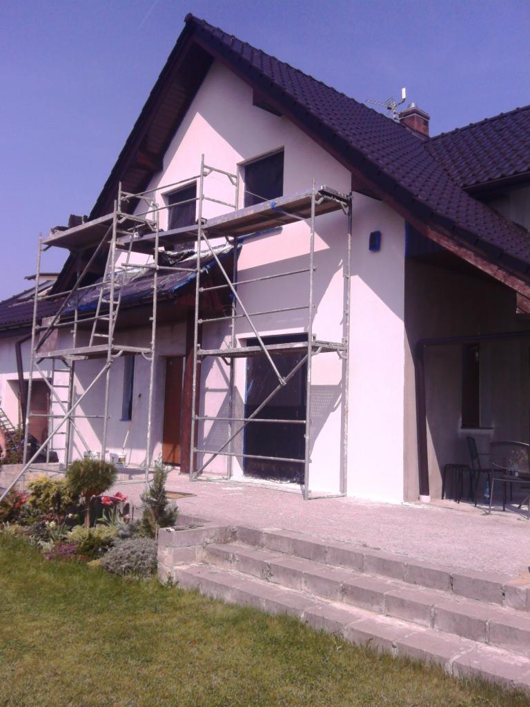 Dom jednorodzinny we Wrocławiu w trakcie malowania elewacji. Widoczne rusztowania i fragment pomalowanej ściany w jasnym odcieniu.