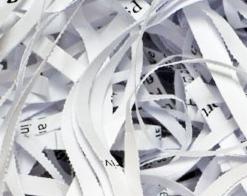 Stos pociętych pasków białego papieru z widocznymi fragmentami zadruku, ukazujący proces niszczenia dokumentów.
