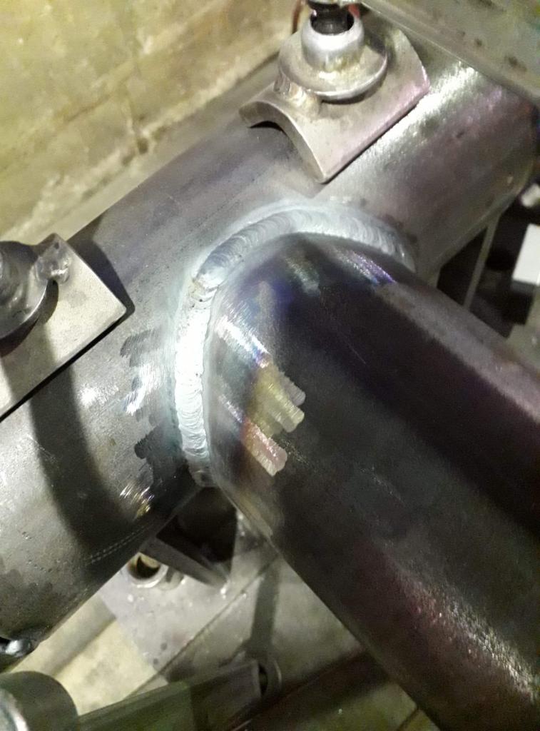 Spoina łącząca dwie metalowe rury, widoczne ślady po spawaniu i mocowania.