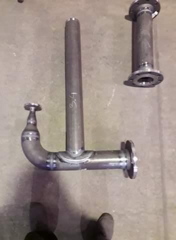 Surowe, spawane metalowe elementy rurowe z kołnierzami, leżące na betonowej podłodze, z widocznymi śladami spawania i napisem '3.4' na pionowej rurze.