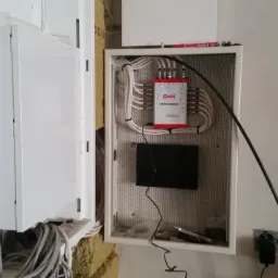 Otwarta skrzynka rozdzielcza z kablami i rozgałęźnikiem sygnału marki Grab's, widoczne kable wychodzące do gniazdka elektrycznego i druga skrzynka obok, ściana w trakcie wykończenia.