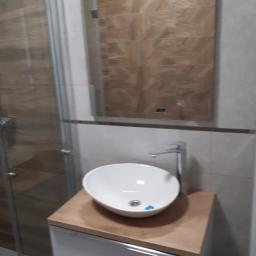 perfektee.pl - Nowoczesna łazienka z owalną umywalką nablatową, bateria chromowana, lustro z dekoracyjnymi płytkami imitującymi drewno i kabina prysznicowa z przesuwnymi drzwiami.