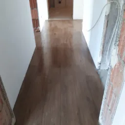 Nowe panele podłogowe w odcieniach brązu, ułożone w korytarzu w Domaniewku, widoczne surowe ściany w trakcie remontu.