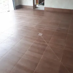 Ułożona, brązowa podłoga z płytek ceramicznych w pomieszczeniu w trakcie remontu, widoczny odpływ liniowy i fragmenty ścian w stanie surowym.