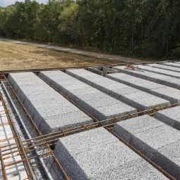 Widok z góry na strop Teriva w trakcie budowy, z widocznym zbrojeniem i betonowymi pustakami, w tle las i pole.