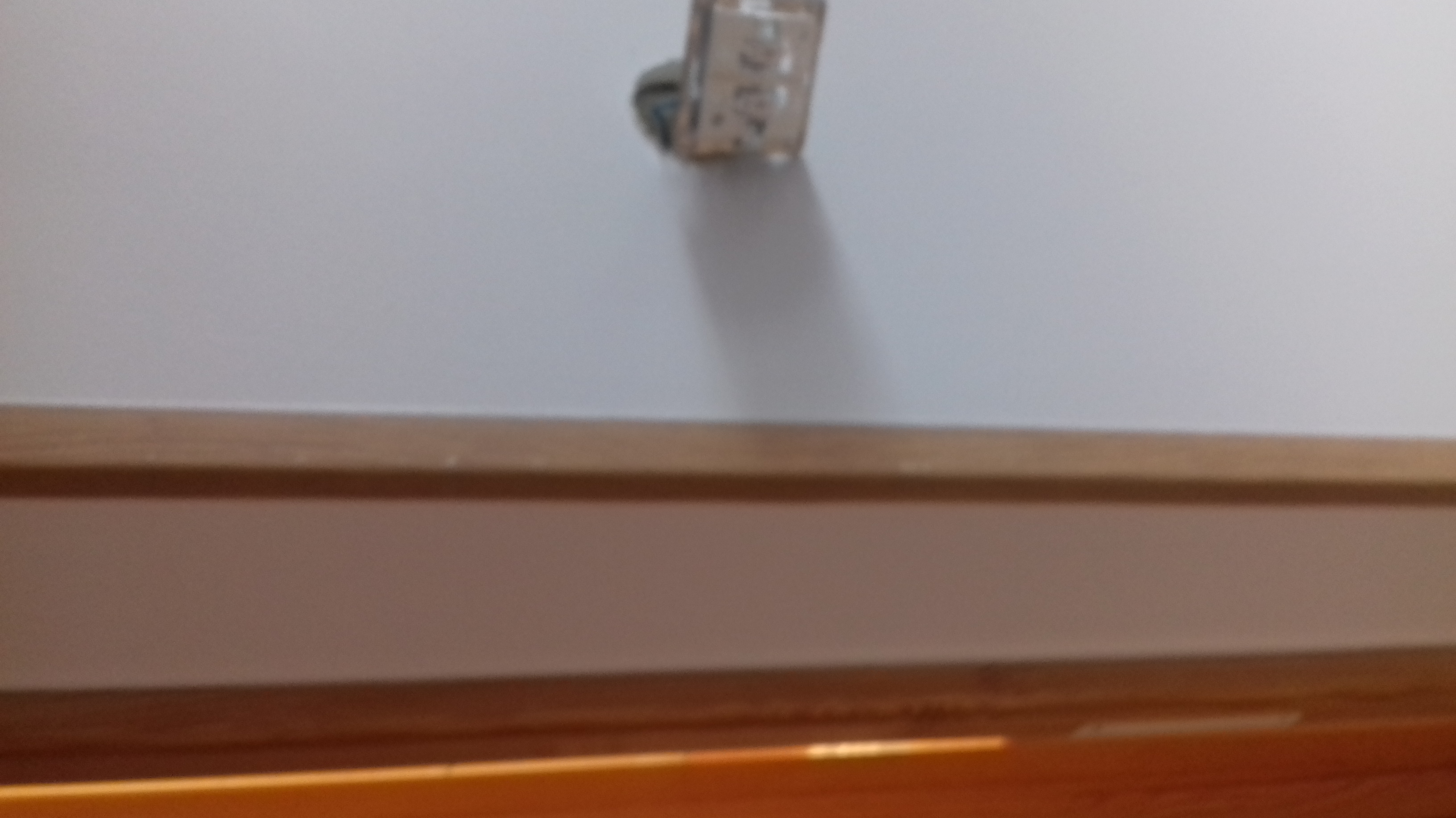 Niedokończone malowanie ściany z widocznym gniazdkiem elektrycznym i drewnianą listwą przypodłogową w dolnej części kadru.