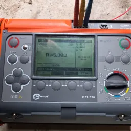 Miernik instalacji elektrycznych Sonel MPI-520 z podłączonymi przewodami pomiarowymi, wyświetlający wynik pomiaru rezystancji uziemienia Re=5,39Ω na tle betonowej posadzki.
