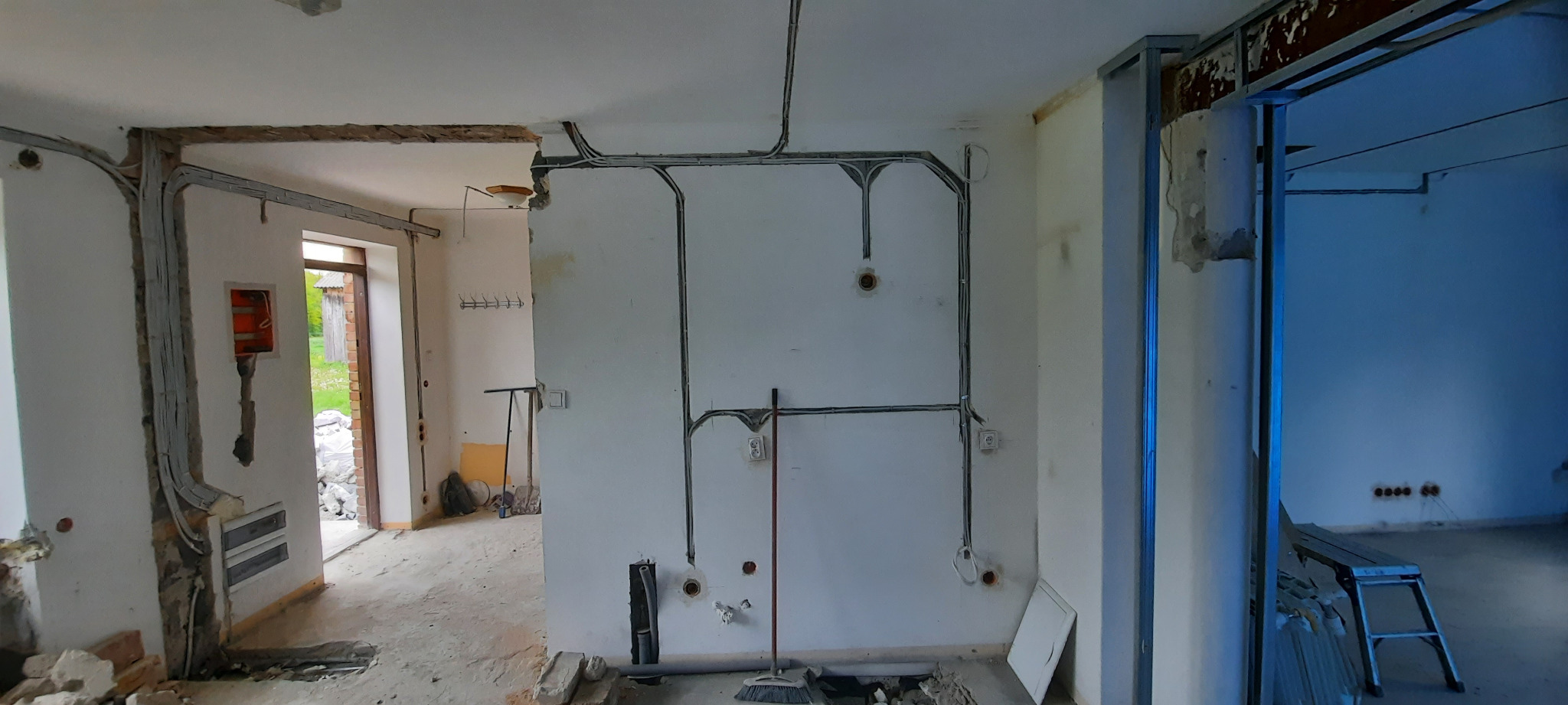 Wnętrze w trakcie remontu z widocznymi przewodami elektrycznymi prowadzonymi natynkowo, puszki instalacyjne w ścianach oraz częściowo otynkowane ściany.