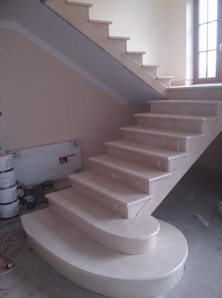 Jasne, zaokrąglone schody wewnętrzne z kamienia, widoczne puszki z farbą i grzejnik w tle, częściowo wykończone wnętrze.