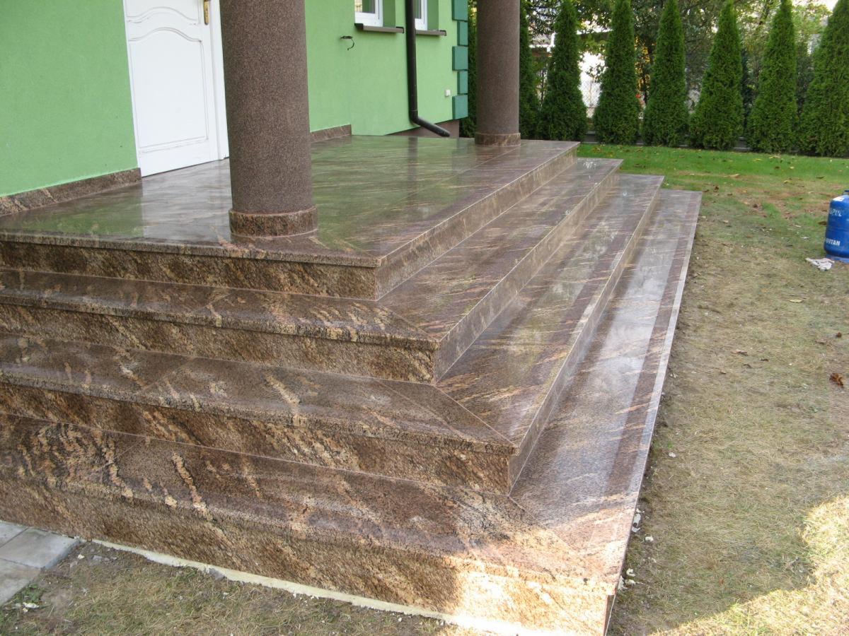 Kamienne schody wejściowe z kolumnami, wykończone brązowym granitem ze wzorem, prowadzące do drzwi budynku z zieloną elewacją.