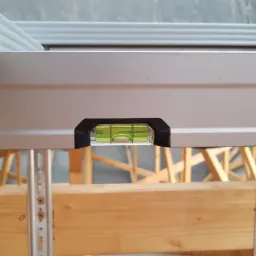 Poziomnica na metalowym profilu konstrukcji sufitu podwieszanego, drewniane elementy konstrukcyjne w tle.