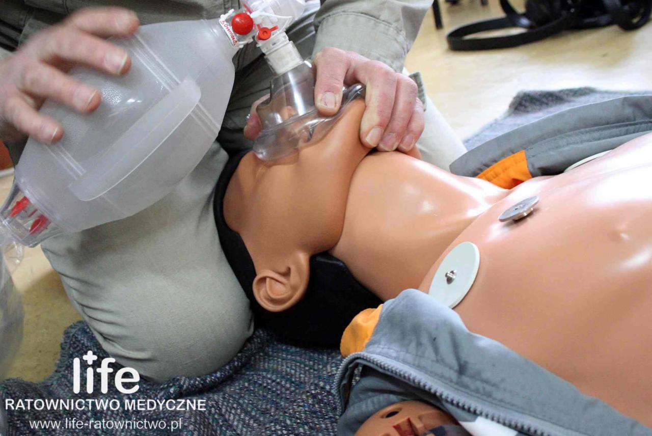 Instruktor demonstruje resuscytację oddechową na manekinie z widocznymi elektrodami EKG i workiem samorozprężalnym z maską twarzową.