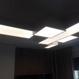 Nowoczesna lampa sufitowa z prostokątnymi panelami LED, asymetrycznie rozmieszczonymi, oświetlająca wnętrze z ciemnymi zasłonami i drewnianą ścianą w tle.