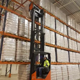 Operator w w&oacute;zku widłowym Linde R16X podnosi paletę z zapakowanymi produktami na wysoki regał w magazynie.