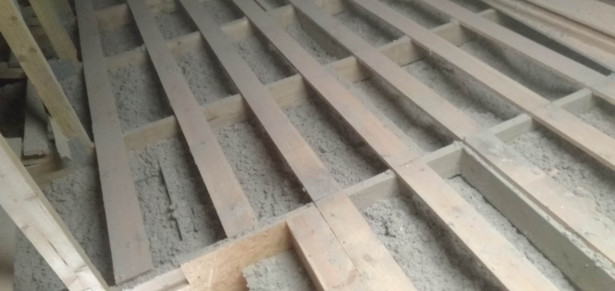 Poddasze w trakcie ocieplania wełną mineralną, widoczne drewniane legary i luźna wełna wypełniająca przestrzeń między nimi.