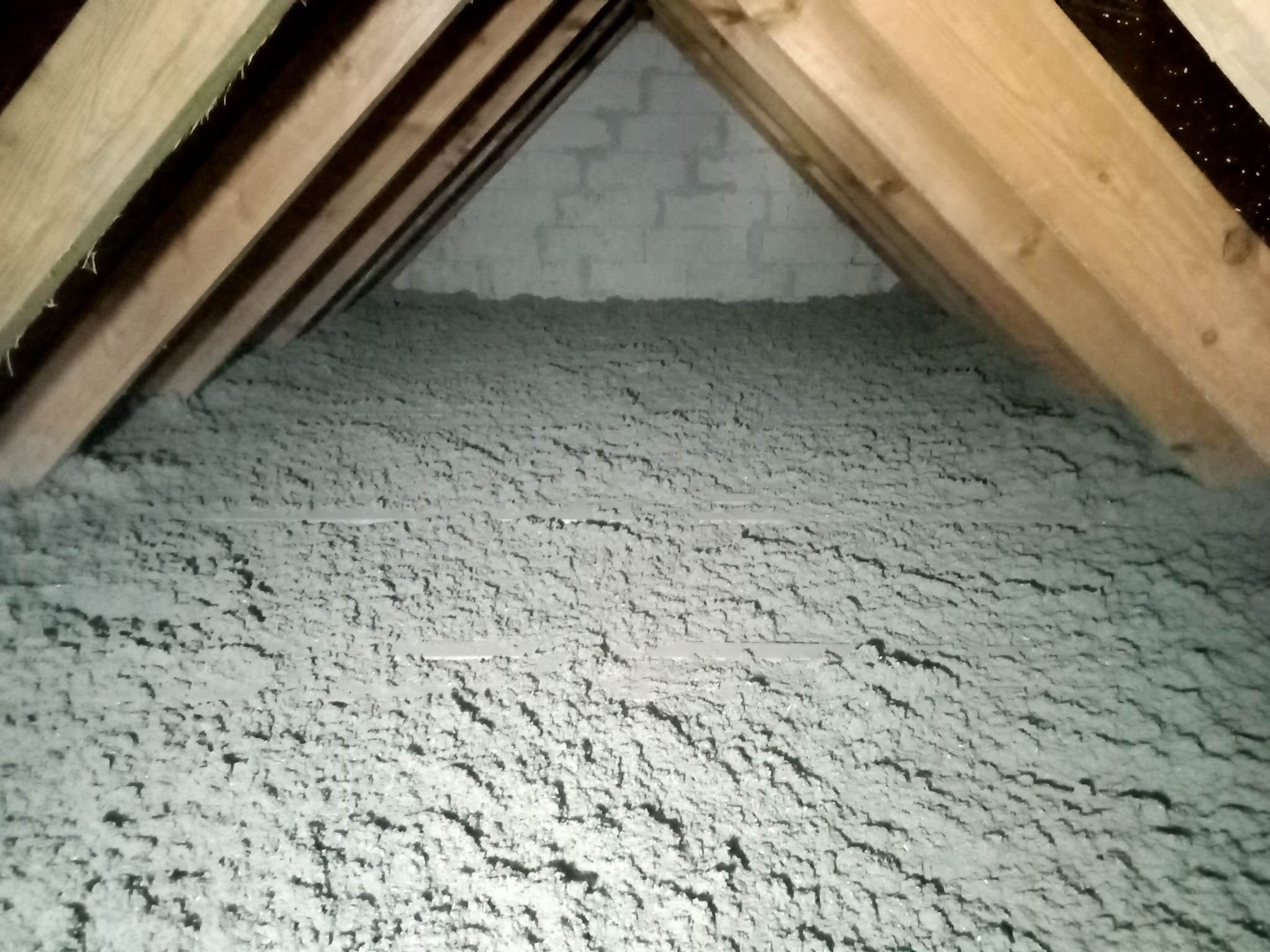 Poddasze z widoczną konstrukcją drewnianą i izolacją z wełny mineralnej, widok z bliska na nierównomierną strukturę izolacji.