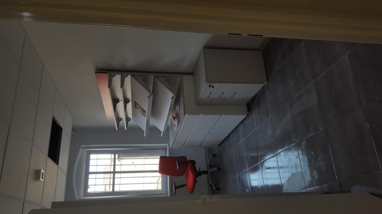 Wykończone wnętrze biura z szarymi płytkami podłogowymi, białymi meblami biurowymi i czerwonym krzesłem obrotowym na tle okna z kratami.