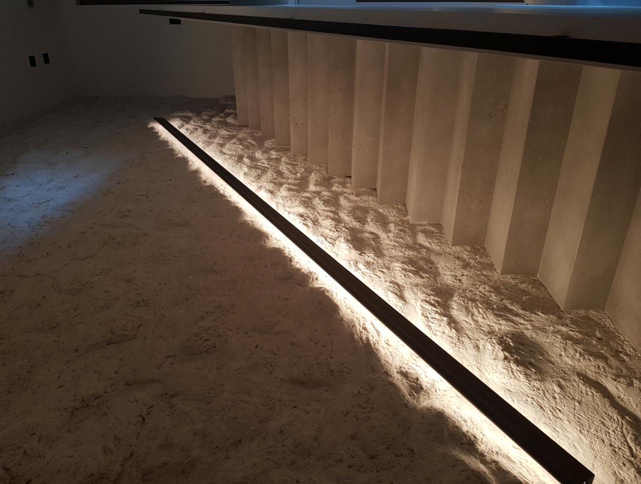 Oświetlenie LED pod schodami, listwa przypodłogowa z wbudowanym światłem, surowy beton, minimalistyczny design.