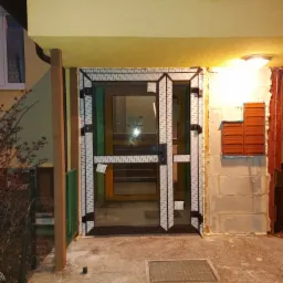 Nowe drzwi wejściowe do klatki schodowej w Żelistrzewie, jeszcze z folią ochronną, widoczne skrzynki pocztowe i tabliczka z nazwą wspólnoty mieszkaniowej.