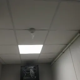 Kasetonowy sufit podwieszany w biurze z widocznymi przewodami i czujnikiem dymu zabezpieczonym folią.