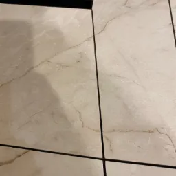 Beżowe płytki podłogowe z marmurkowym wzorem i czarnymi fugami, ułożone w regularny wzór, widoczne z bliska.