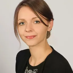 Portret kobiety o jasnych oczach i brązowych włosach, ubrana w czarną bluzkę z białym haftem, na neutralnym tle.