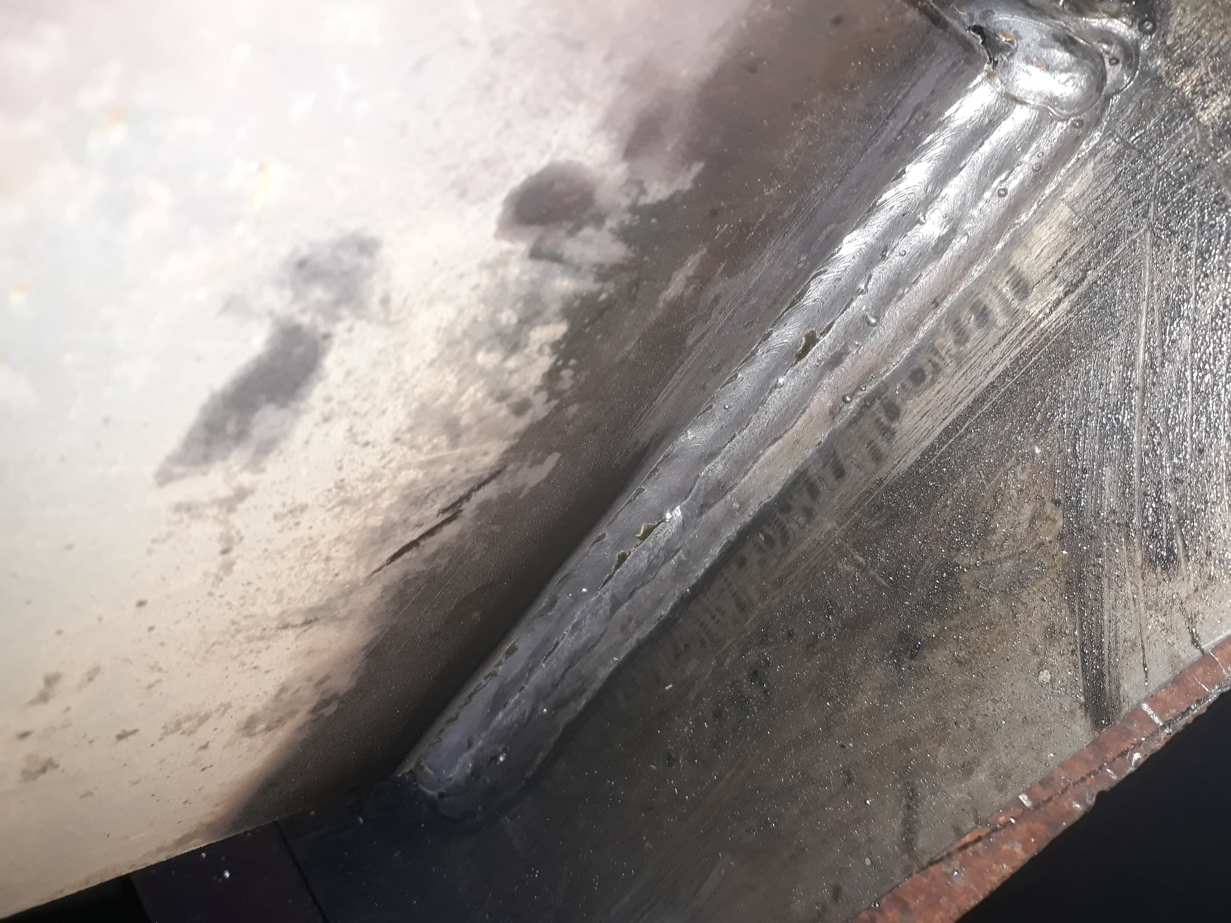 Spoina łącząca dwie metalowe powierzchnie pod kątem, widoczne ślady po spawaniu i chropowata faktura metalu.