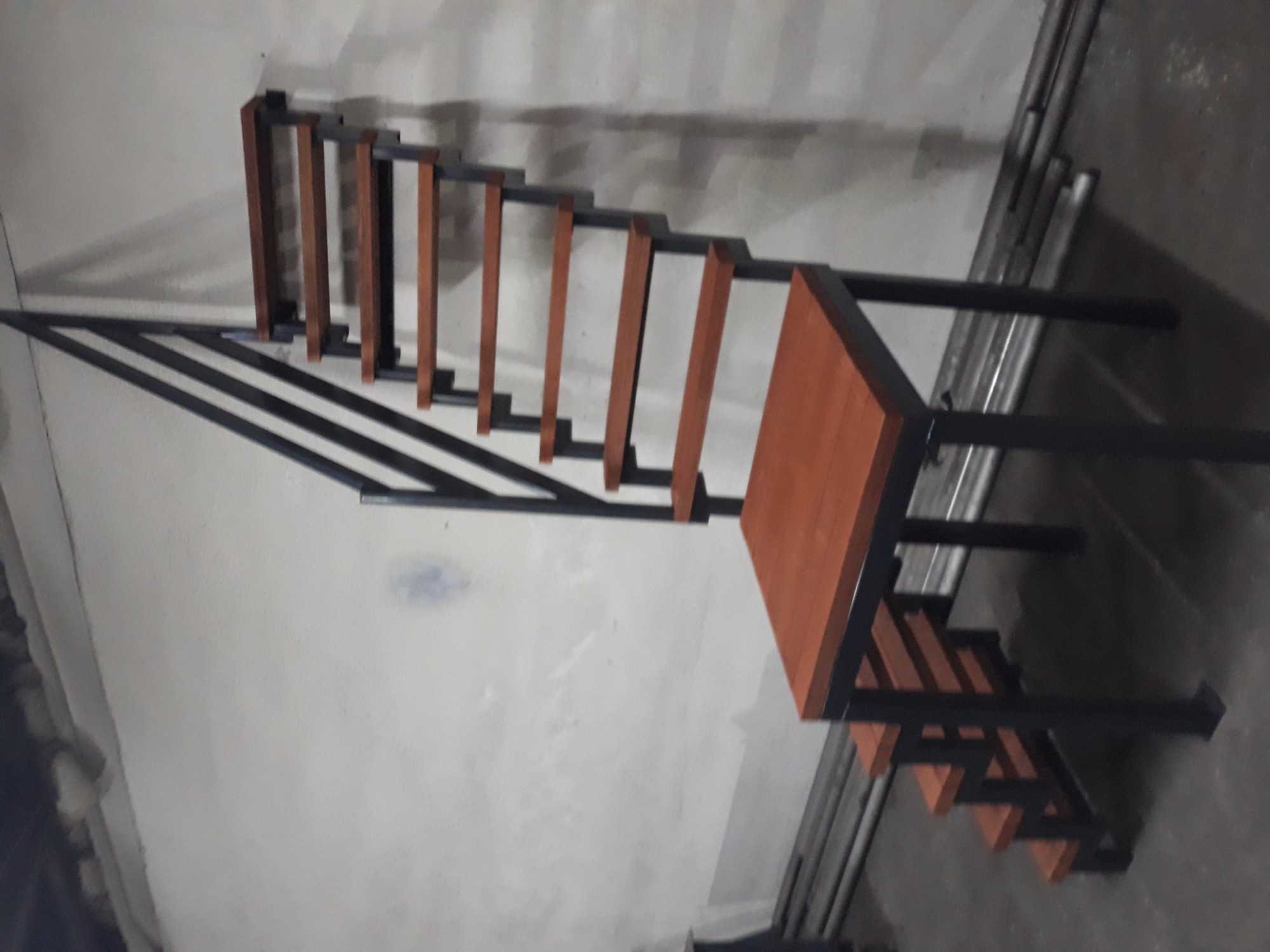 Schody metalowe z drewnianymi stopniami, malowane proszkowo, z widoczną konstrukcją i sklejkowymi stopniami zaimpregnowanymi lakierem, ustawione w surowym wnętrzu.