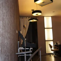 Nowoczesne wnętrze po remoncie: ściana z dekoracyjną tapetą, oświetlenie punktowe z lampami wiszącymi, jasne panele ścienne, krzesło biurowe i czerwony fotel.