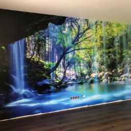 Fototapeta z motywem wodospadu i lasu na ścianie, widoczne gniazdka elektryczne, ciemna podłoga.