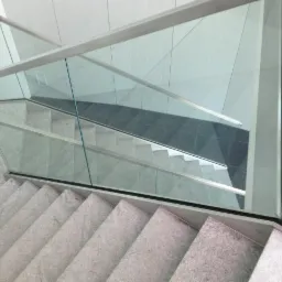 Wewnętrzne schody wykończone szarym kamieniem, zabezpieczone przezroczystą taflą szkła z metalową ramą i poręczą, widok z góry.