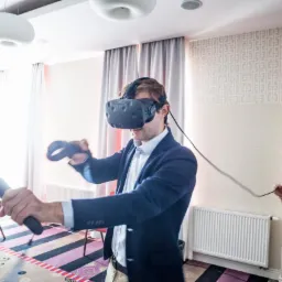 Mężczyzna w garniturze używa zestawu VR HTC Vive w jasnym pomieszczeniu z wzorzystą tapetą, kobieta trzyma kabel.