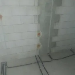 Surowy mur z betonu komórkowego z widocznymi puszkami instalacyjnymi i poprowadzonymi przewodami elektrycznymi w peszlach, w trakcie montażu.