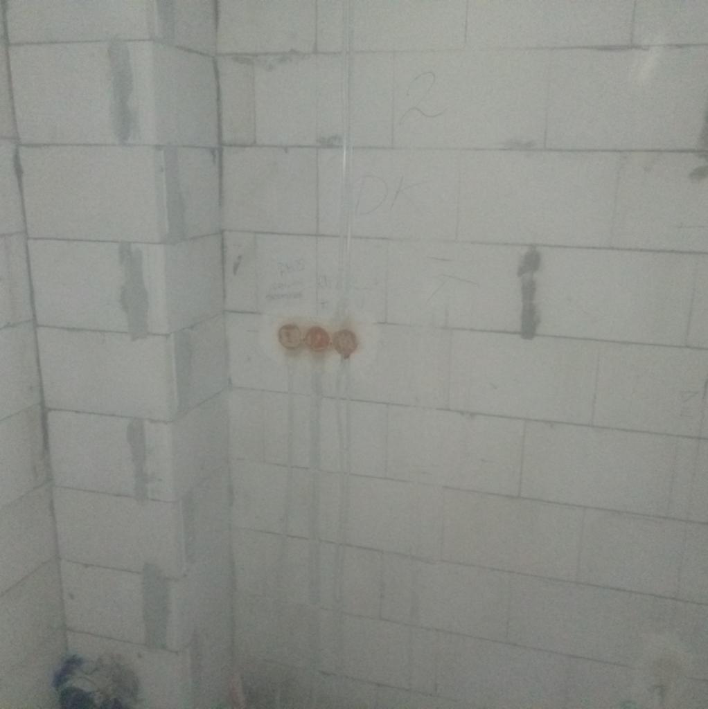 Ściana z betonu komórkowego z trzema okrągłymi puszkami instalacyjnymi w kolorze ceglastym, z których zwisają przewody. Na ścianie widoczne napisy ołówkiem.