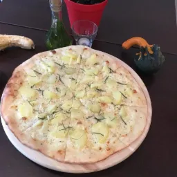 Pizza z ziemniakami i rozmarynem na drewnianym talerzu, dekorowana małymi dyniami i oliwą w ozdobnej butelce.