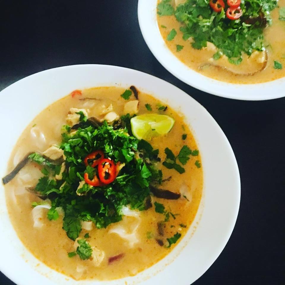 Dwie miski tajskiej zupy Tom Yum z kurczakiem, grzybami, kolendrą, papryczką chili i ćwiartką limonki, na czarnym tle.