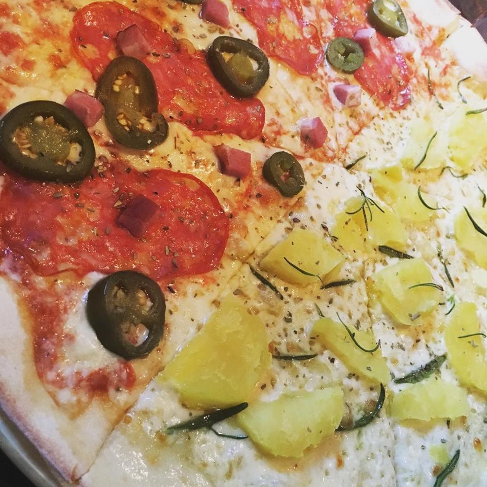 Pizza podzielona na dwie części: jedna z salami, jalapeno i kostkami szynki, druga z ananasem i ziołami, widok z góry.