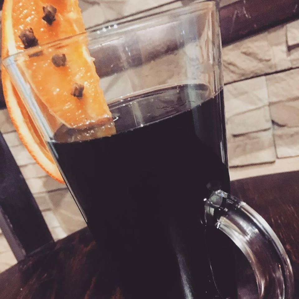 Grzane wino w szklance z pomarańczą i goździkami na drewnianym stole, tło imitujące kamień.