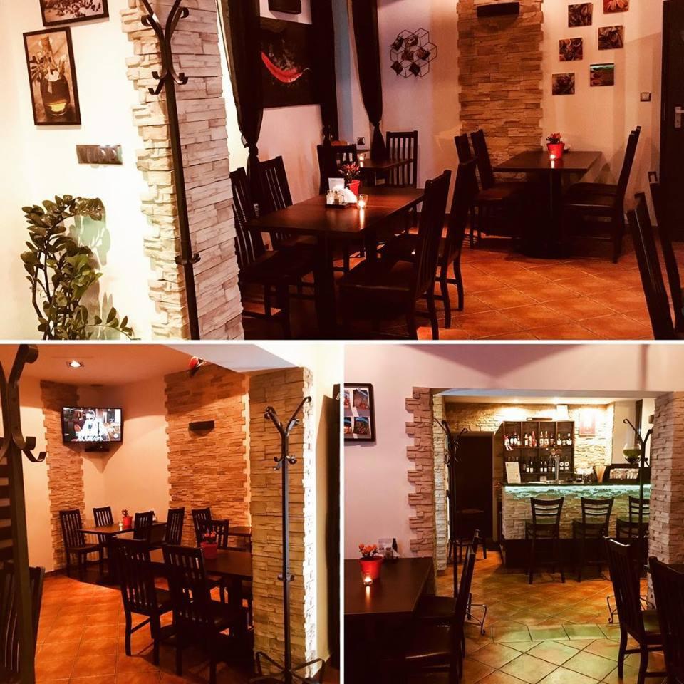 Wnętrze restauracji z dekoracyjnymi ścianami z kamienia, ciemnymi drewnianymi meblami i barem w tle, tworzące przytulną atmosferę.