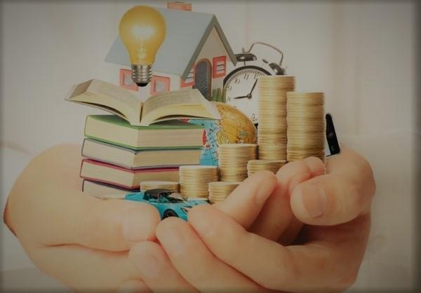 Dłonie trzymające stos książek z otwartą książką na wierzchu, model domu z żarówką, stosy monet, globus, zegar i model samochodu.