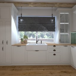 Projekt Studio Dagmara Hus - Jasna kuchnia w stylu rustykalnym z drewnianymi belkami stropowymi, białymi szafkami z ciemnymi uchwytami, dużym oknem z roletą rzymską i widokiem na ogród, oraz ceramicznym zlewozmywakiem.