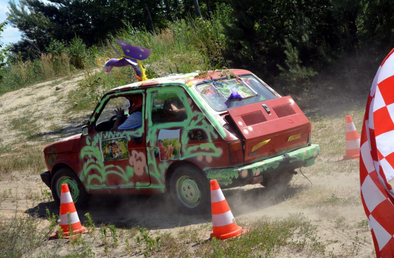 Modyfikowany Fiat 126p z zielonymi graffiti i fioletową dekoracją na dachu, pokonujący tor przeszkód z pachołkami.